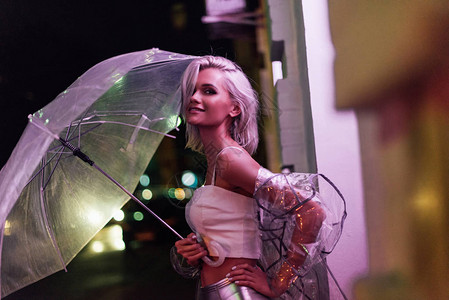 穿着透明的雨衣晚上在红光下带着雨伞在街上露着笑图片