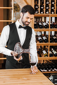英俊的年轻侍酒师在葡萄酒店从醒酒器中倒酒图片