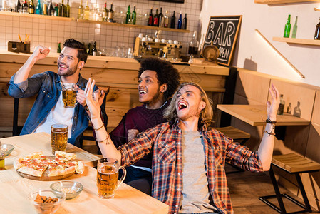 年轻朋友在喝啤酒吃比萨看酒吧足球比赛的同时图片