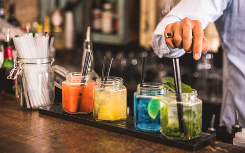 在时尚鸡尾酒吧的老式玻璃杯上用吸管的五彩时尚饮料的调酒师手图片
