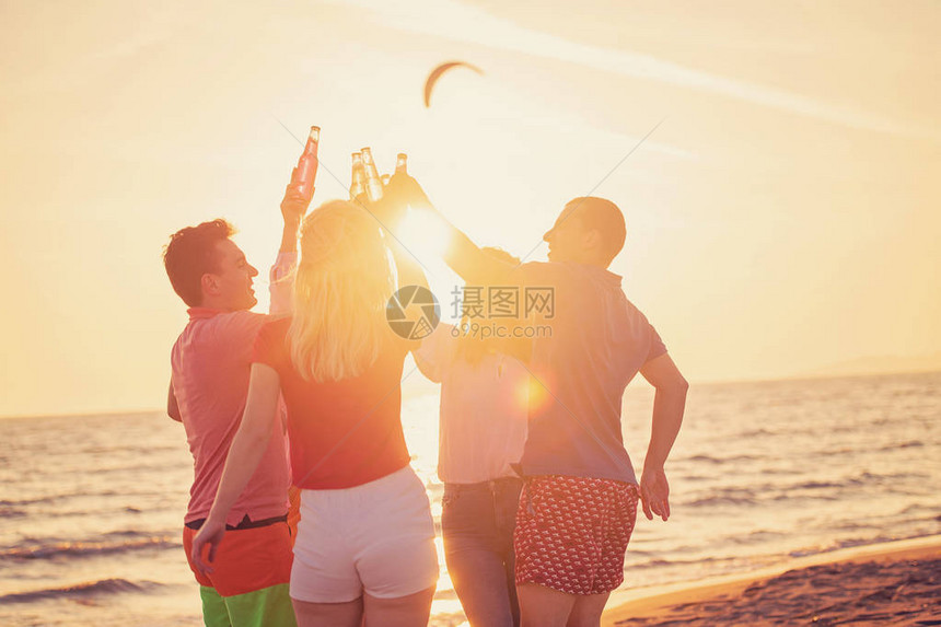 一群快乐的年轻人在美丽的夏日夕阳下在海图片
