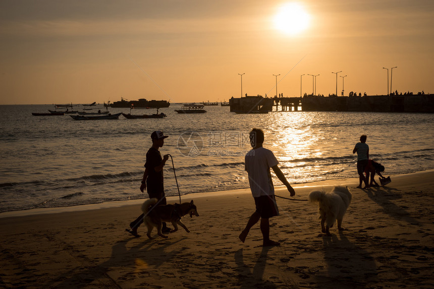 日落时人们在海滩上走狗的轮廓渔船靠图片