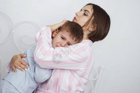 年轻漂亮的女人和儿子穿着粉色和蓝色的睡衣躺在床上图片