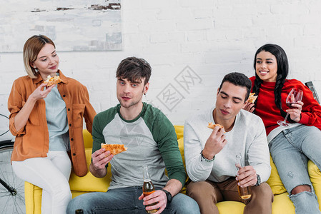 快乐的多元文化朋友一起坐在黄色沙发上吃披图片