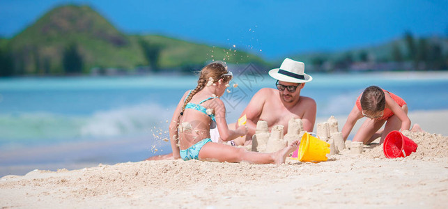 父亲和两个孩子玩沙子在热带海滩上图片