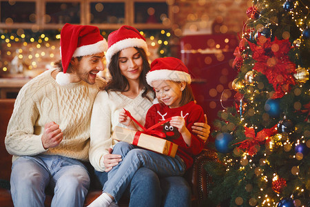 可爱的节日小女孩在圣诞节前夕与妈和爸一起打开圣诞礼物图片