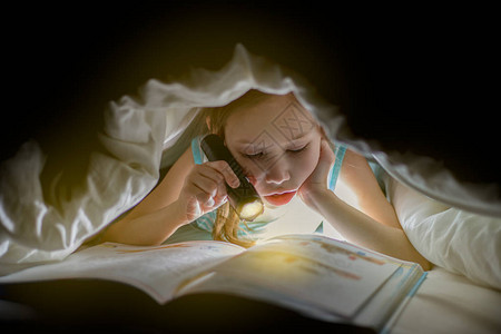 修女在用手电筒的毯子下看一本书漂亮的年轻女孩在儿童室玩得开背景图片