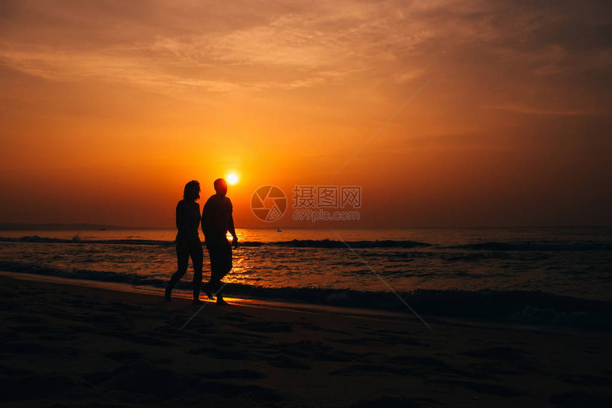 一对在海边滩相爱的情侣的背影在夏天橙色图片