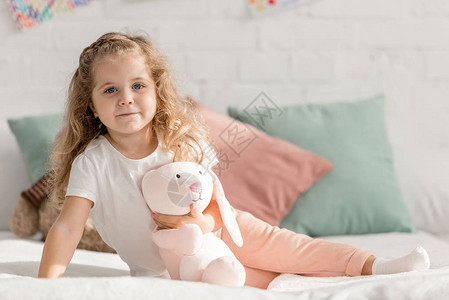 可爱的小孩坐在床上和玩具在儿童室图片