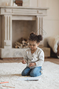 可爱的非洲小女孩用铅笔画坐在家里地毯上背景图片