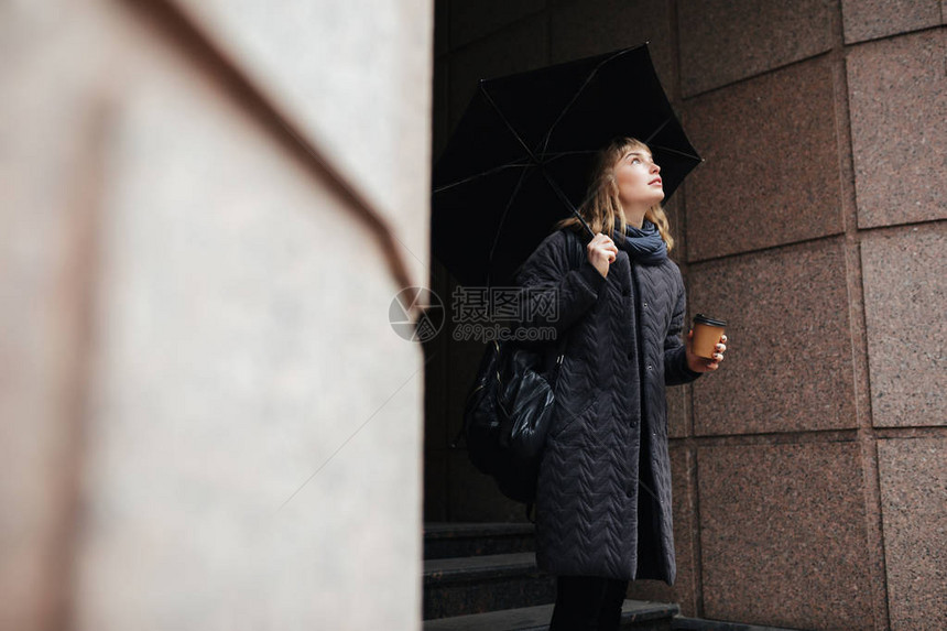 美丽的女士的肖像站在街上拿着黑色雨伞和咖啡图片