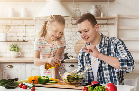 积极的爸和小女儿在家里的厨房做饭男人教女孩添加适量的沙拉背景