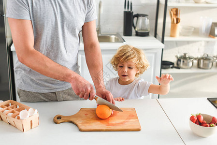 男人用刀砍橙子和儿子站在厨房旁图片