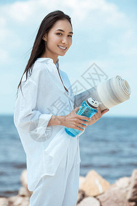 在海滩上拿着一瓶水和瑜伽垫子的运动用品瓶背景图片
