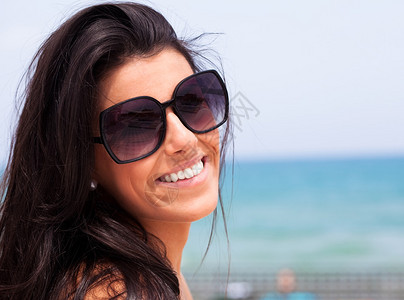穿着墨镜与海滩相伴笑脸的漂亮年轻女图片