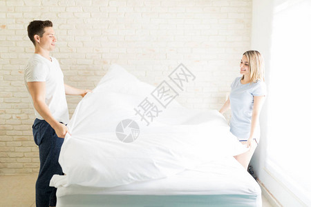 恋人在公寓的床上整理白色床单图片