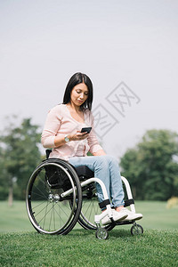 在公园休息时使用智能手机坐在轮椅上的漂亮残图片