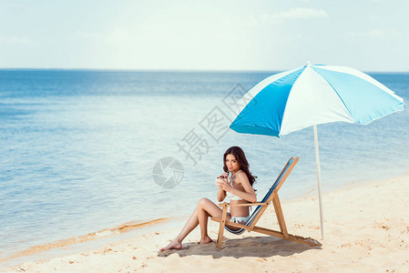 穿着比基尼酒椰子鸡尾酒的年轻女子在海滩上图片