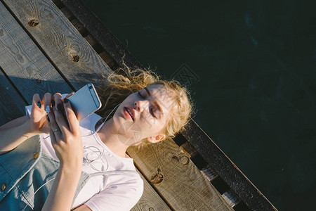 年轻漂亮的金发女孩少年躺在海边的码头上图片