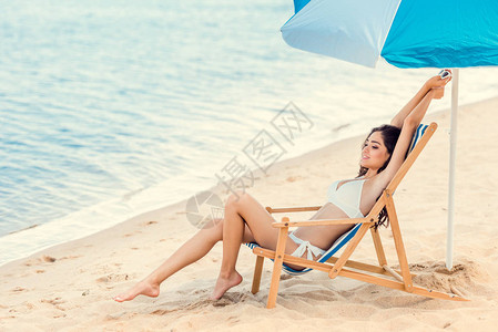 快乐的女孩在海边的太阳伞下坐图片