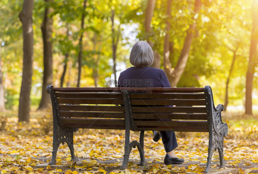 老妇人坐在秋天公园的长椅上的老妇人坐在秋天公园的图片