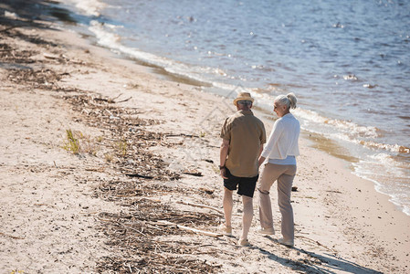 河边牵手走在沙滩上的老年夫妇的背影图片