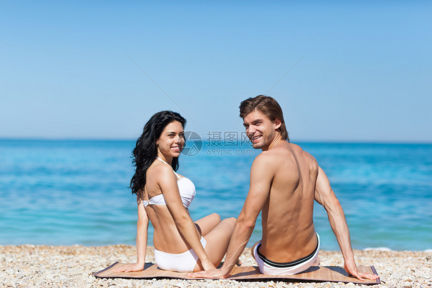 坐在沙滩上看着相机的情侣的后视图图片