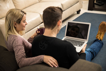 目睹一对年轻夫妇在家里一台笔记本电脑上观看电图片
