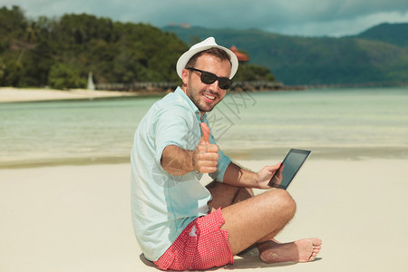 男人在坐沙滩上时笑着举起拇指并用图片