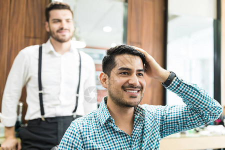 英俊的年轻客户在店里检查新剪的头发和有理发师背景图片