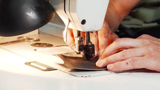 一位成熟的专业鞋匠在他的工作室使用老式缝纫机处理皮革的裁剪镜头制作手工鞋的工背景图片