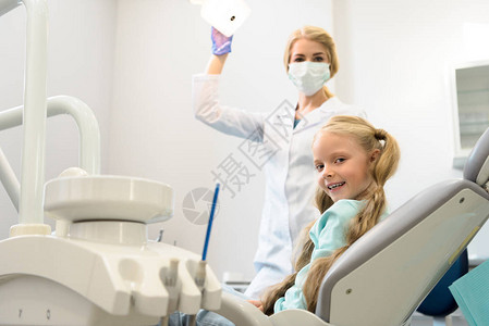 快乐的小孩在牙医办公室坐在椅子上看着照图片