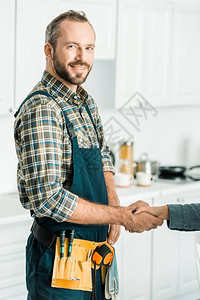 微笑英俊的水管工和顾客在厨房里握手图片
