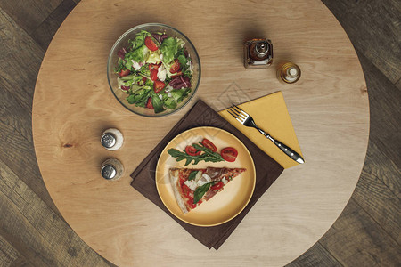 盘子里的披萨碗里的沙拉和木质表面的香料的顶部视图图片