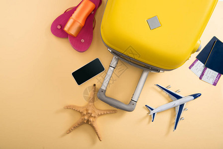 黄色手提箱飞机模型海星防晒霜人字拖智能手机和米色背景的图片