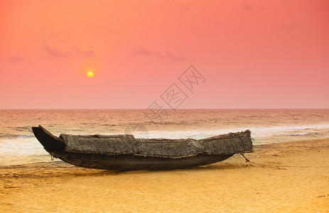 太阳落在一艘搁浅的印度喀拉邦传统渔船后面船上覆盖着椰子棕榈茅背景图片
