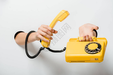 妇女通过白色洞口持反黄色固定式电话的妇女的作物图象背景图片