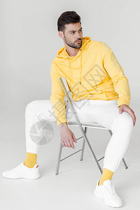 穿着黄连帽衫和白裤子的时尚年轻男子坐背景图片