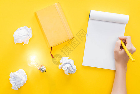 妇女写在空白笔记本碎纸球和黄色背景的灯泡上图片