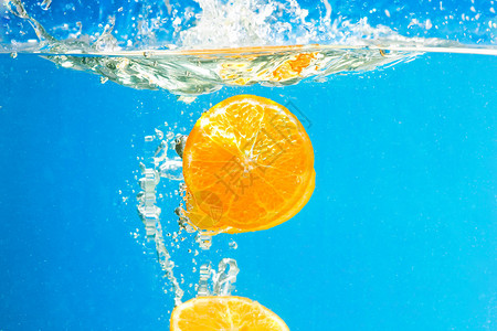 蓝色背景水中溅起的柑橘片背景图片