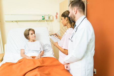 高级病人与男女保健工作者交谈时站在医院床上的床背景图片