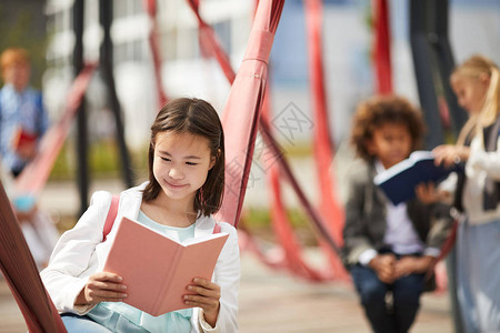 亚洲女学生在学校操场户外阅读书图片