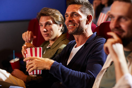 一群笑着的男人在电影院看电影和吃爆米花图片
