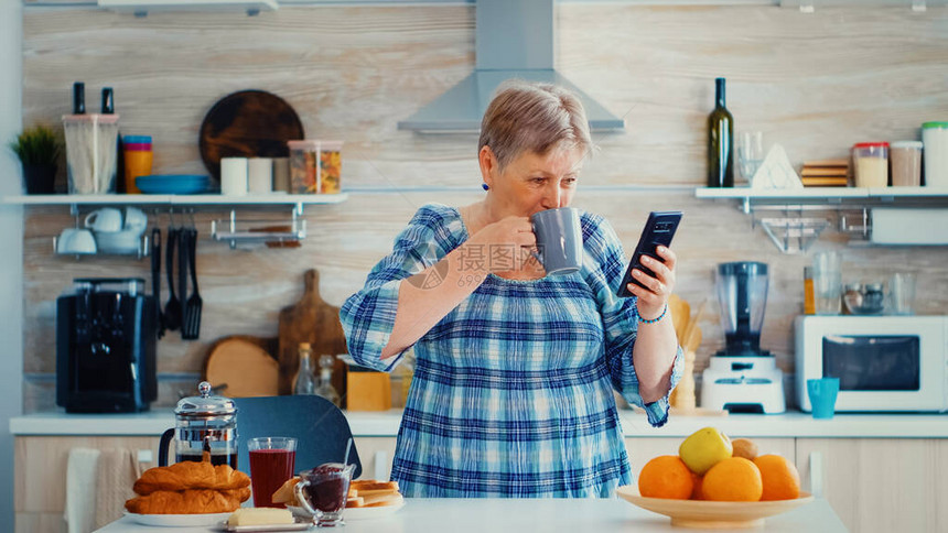 高龄妇女在厨房早餐时享受智能手机音乐图片