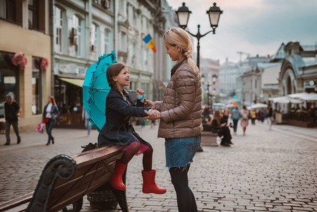 撑着蓝色雨伞的小女孩坐在莫斯科的长椅上和妈妈一起玩图片