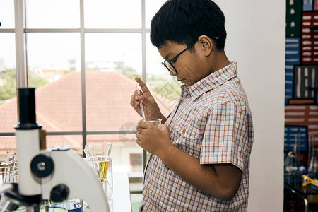 实验室里戴眼镜的亚洲小男孩拿着烧杯的特写图片
