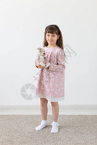 美丽的小女孩拿着一只穿着粉色连衣裙的泰迪兔图片