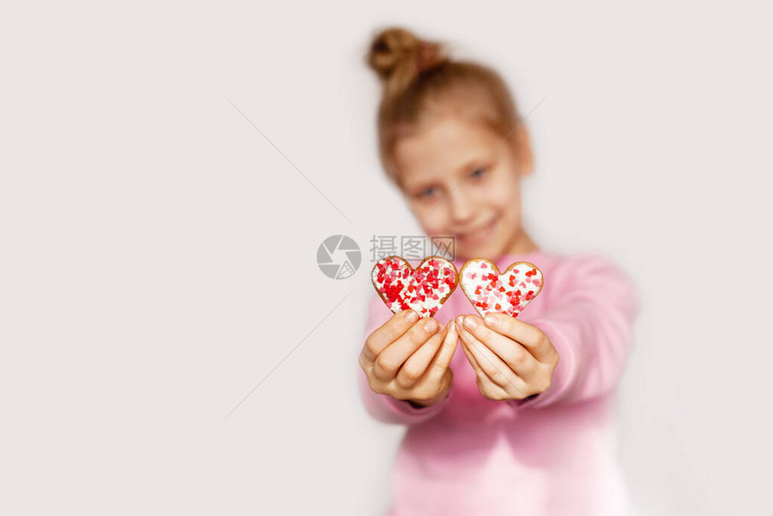 一个快乐的女孩拿着红心形的姜饼可爱女孩的肖像与饼干一起在浅色背景和图片