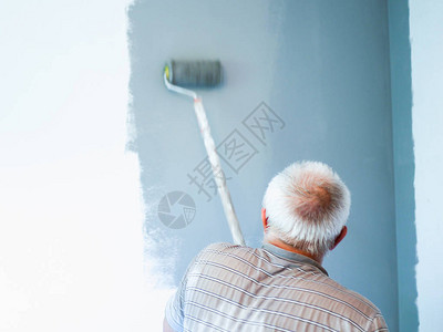 一位老人用滚筒刷墙老人进行维修用滚筒粉刷墙壁旧衣服白墙上的灰色图片
