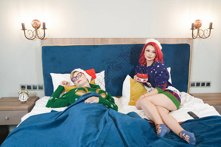 两个睡不着的疲倦朋友穿着圣诞毛衣一起在床上休图片